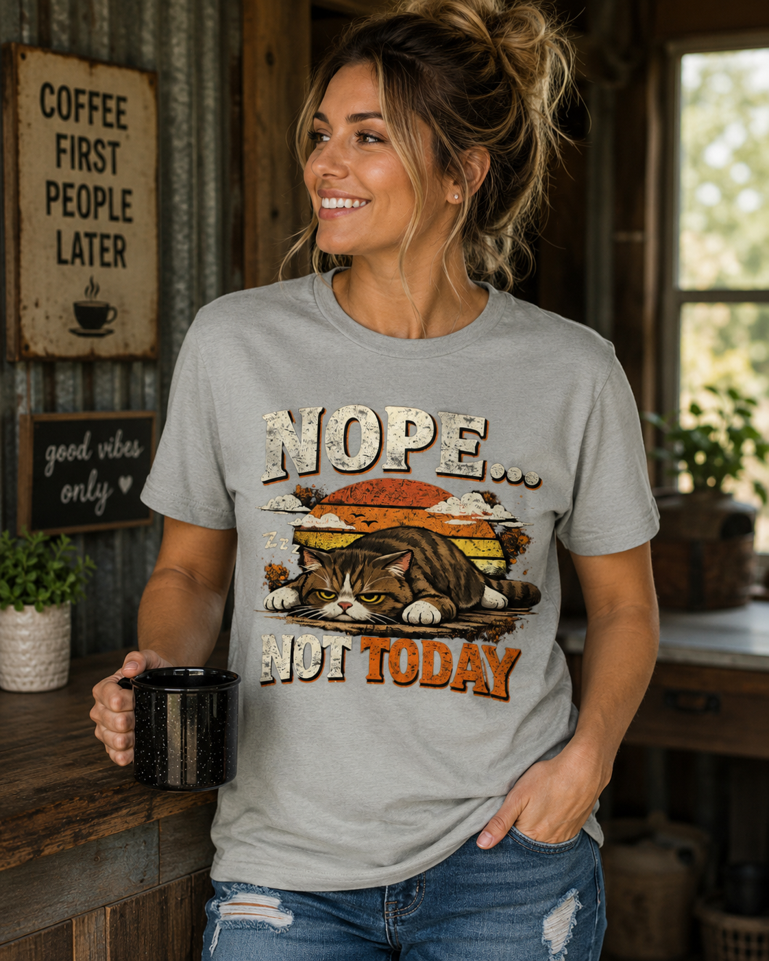 Woman wearing a gray t-shirt with a cat graphic and text in a rustic indoor setting.
